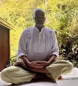 balance masculine and feminine energy meditation practice - David in crossed legged sitting and hands on top of each other with greenery behind him 